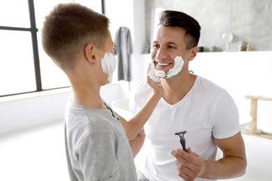 Photo of Son applying shaving foam onto father's face in bathroom