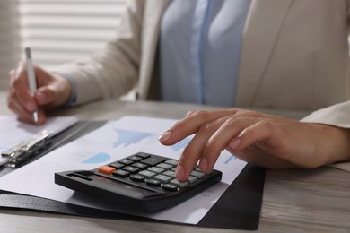 Photo of Woman using calculator at light wooden table in office, closeup