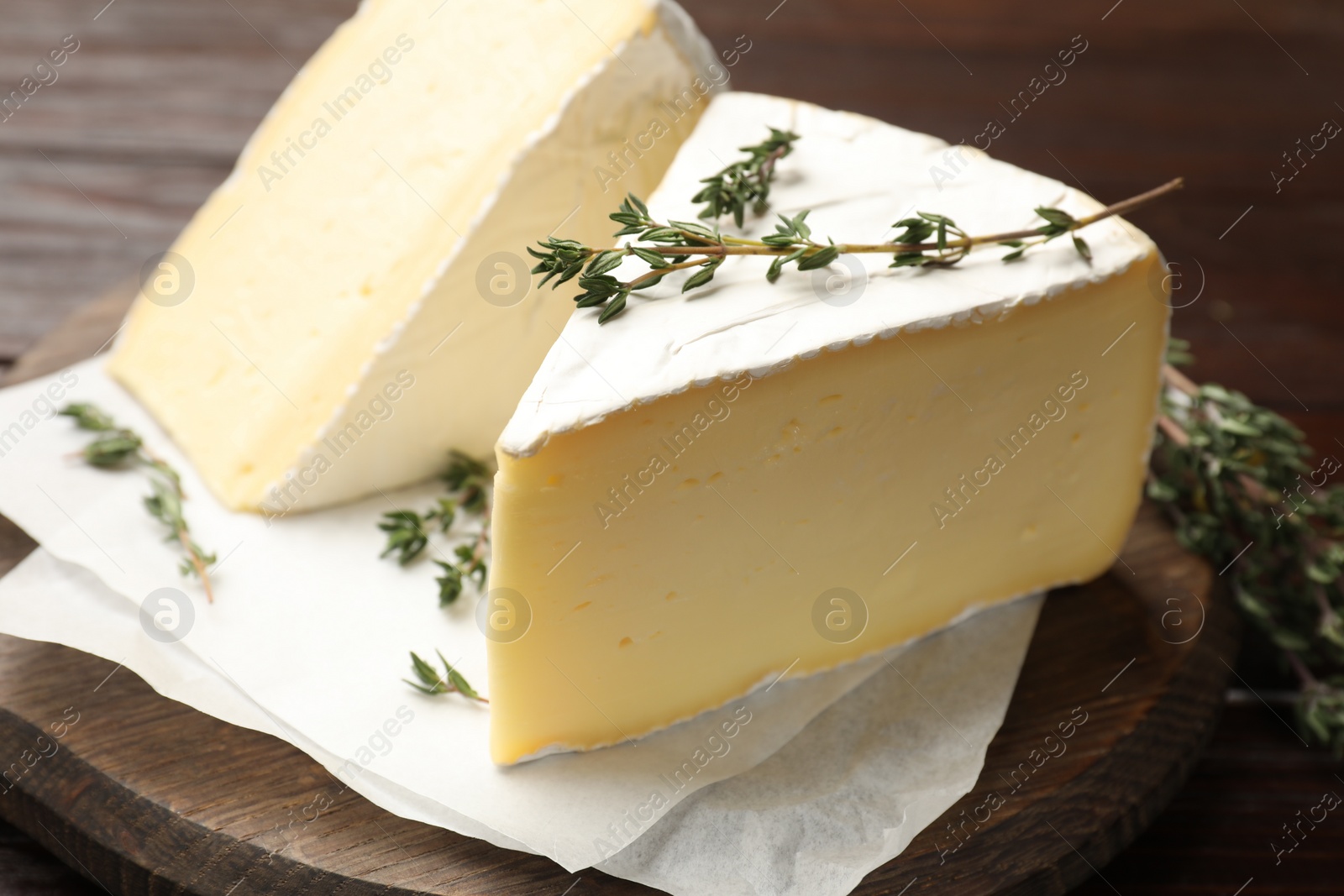 Photo of Pieces of tasty camembert cheese and thyme on wooden table, closeup