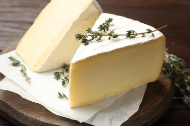 Photo of Pieces of tasty camembert cheese and thyme on wooden table, closeup