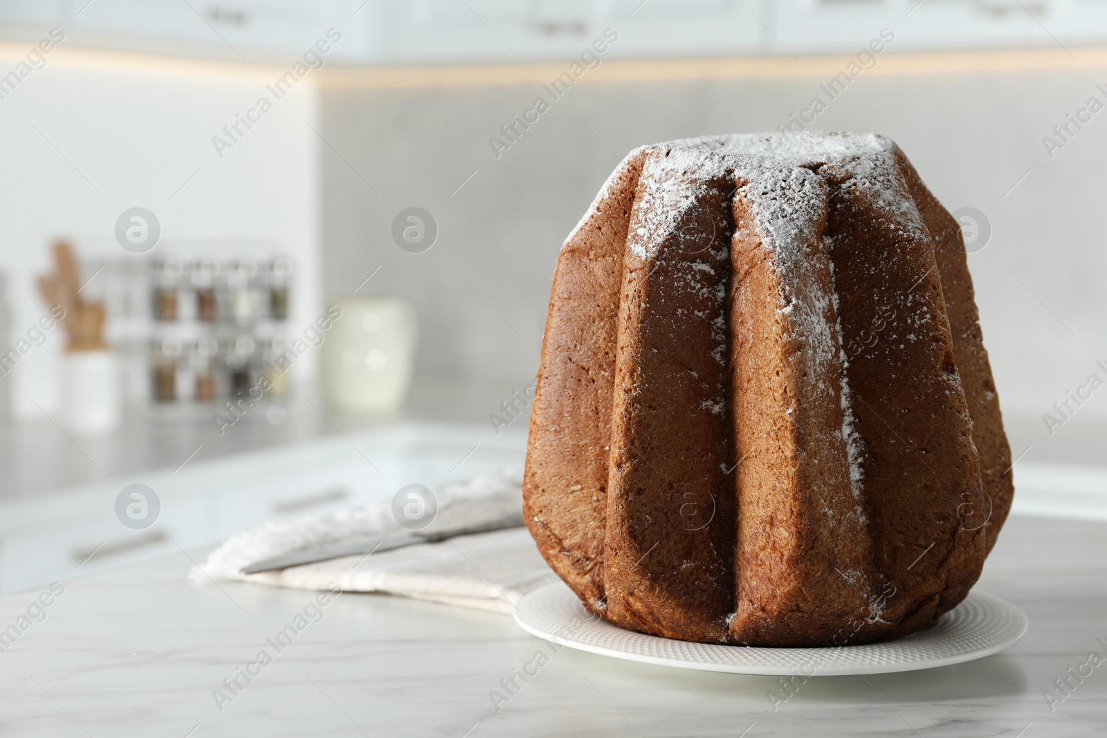Photo of Delicious Pandoro cake decorated with powdered sugar on white table in kitchen, space for text. Traditional Italian pastry
