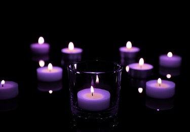 Burning violet candle on black background, closeup. Funeral attributes