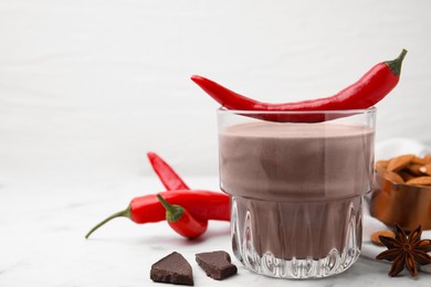 Photo of Glass of hot chocolate with chili pepper on white marble table. Space for text