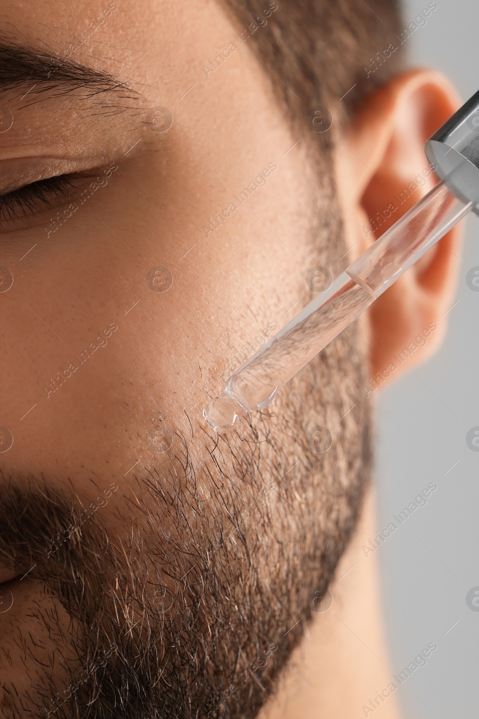 Photo of Man applying cosmetic serum onto face, closeup