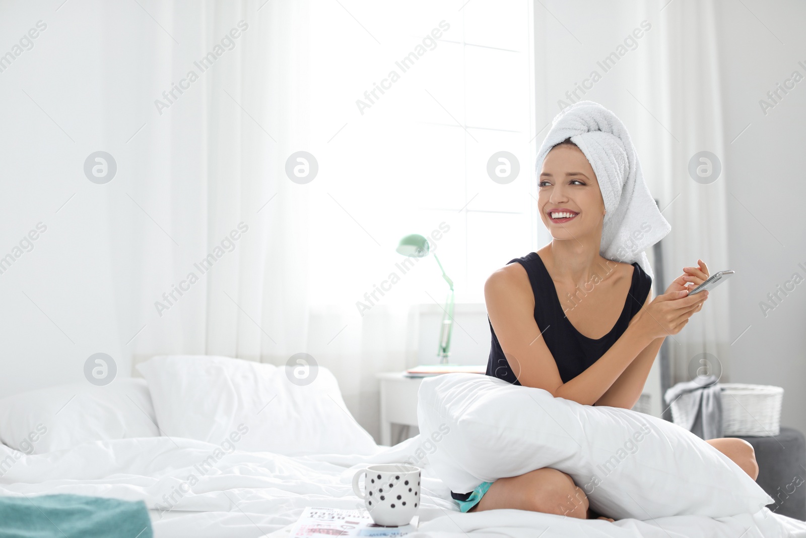 Photo of Young happy woman with mobile phone on bed at home. Lazy morning