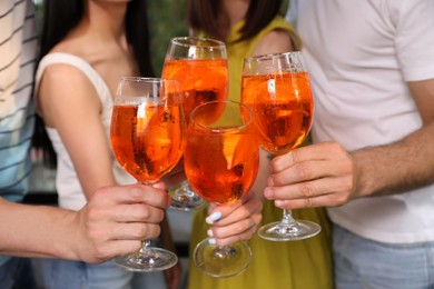 Photo of Friends clinking glasses of Aperol spritz cocktails outdoors, closeup