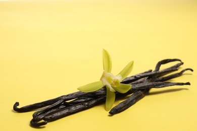 Photo of Vanilla pods and beautiful flower on yellow background. Space for text
