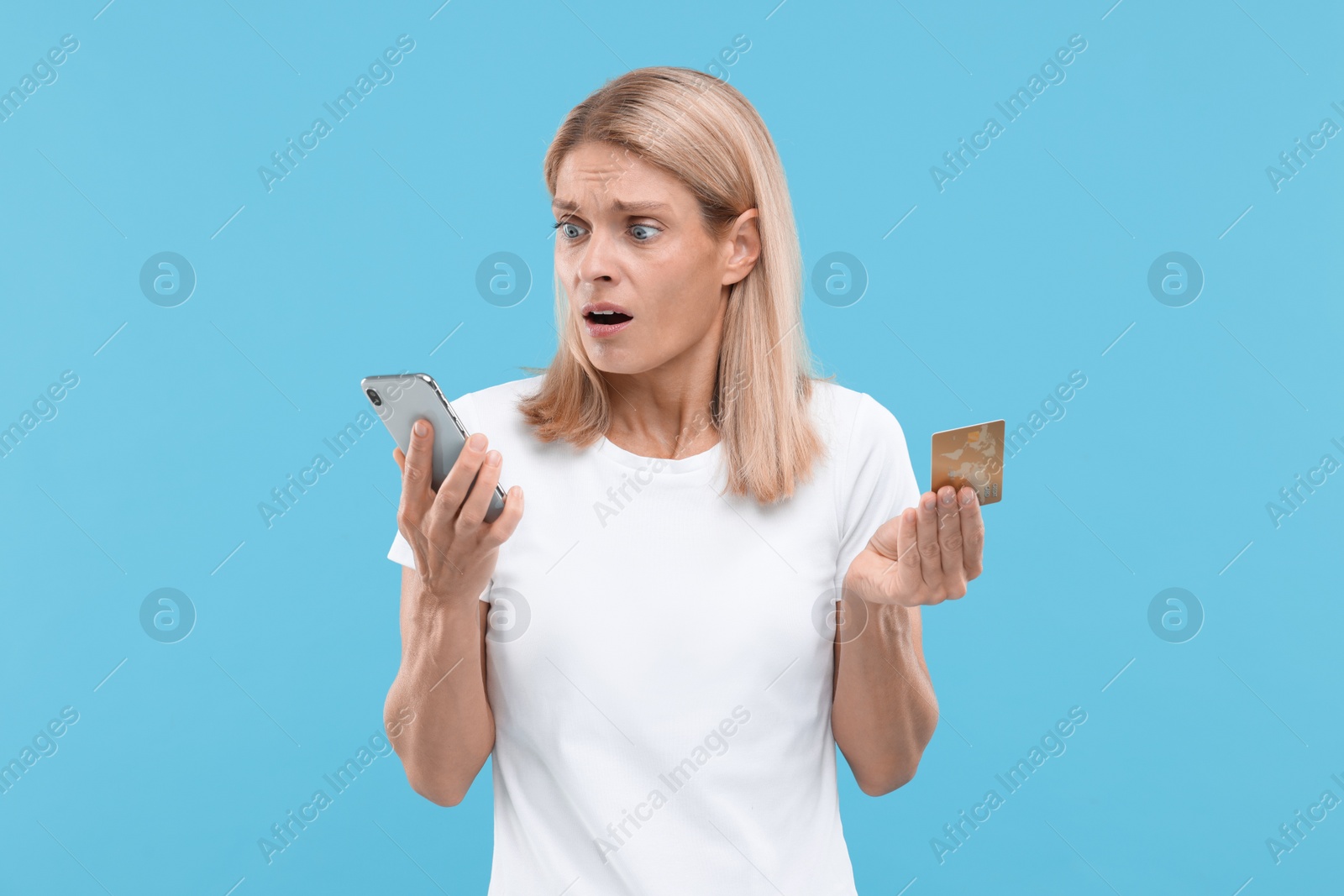 Photo of Stressed woman with credit card and smartphone on light blue background. Be careful - fraud