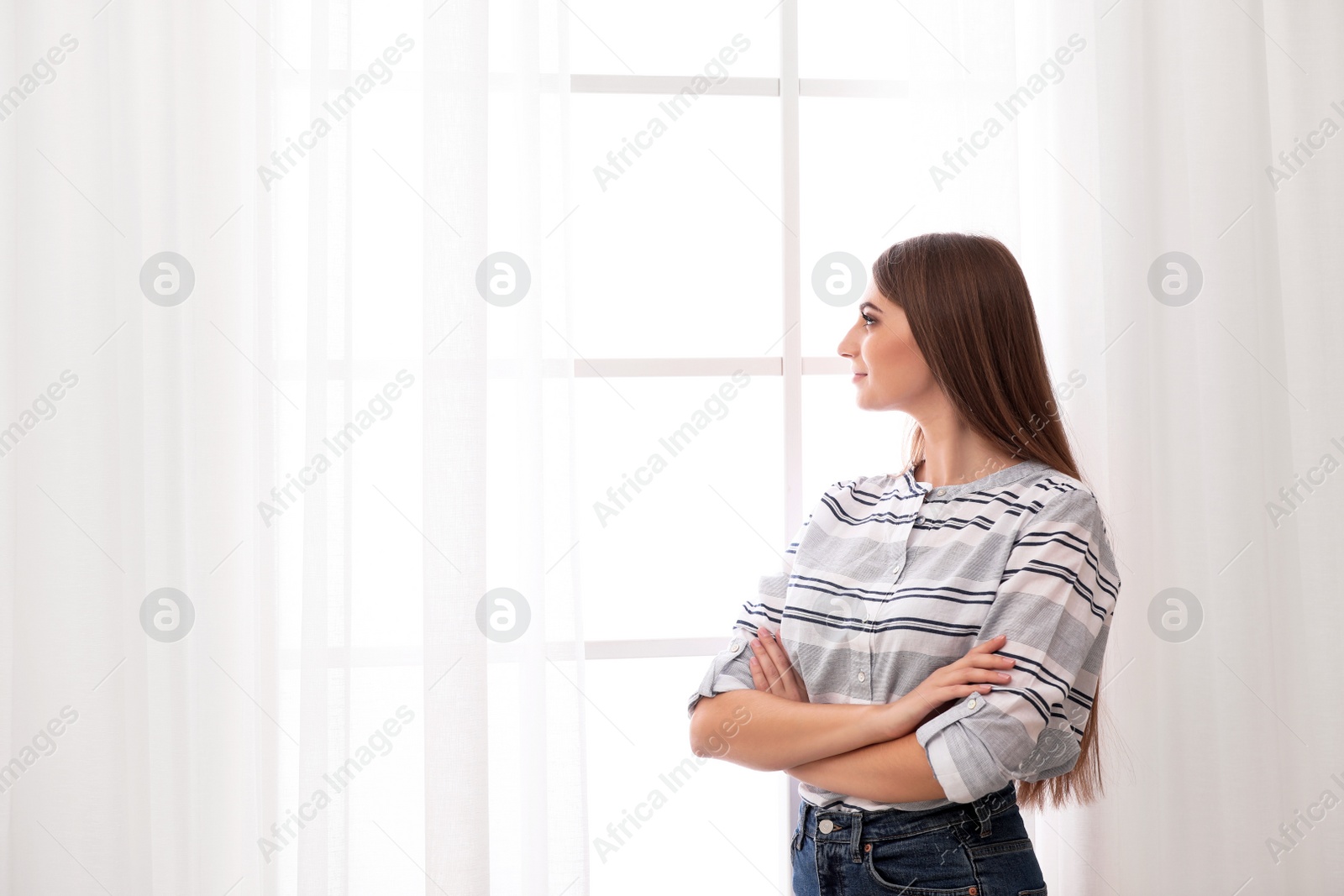 Photo of Young woman near window with open curtains at home. Space for text