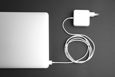 Photo of Laptop and charger on black background, flat lay. Modern technology