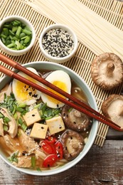 Photo of Noodle soup. Bowl of delicious ramen, ingredients and chopsticks on wooden table, flat lay