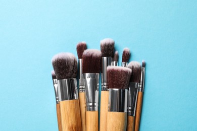 Different makeup brushes on light blue background, flat lay. Space for text