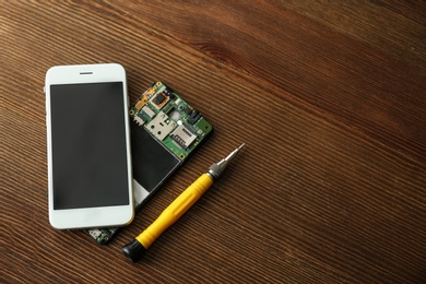 Flat lay composition of mobile phones and screwdriver on wooden table, space for text. Repairing service