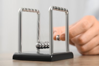 Photo of Man playing with Newton's cradle at table against light background, closeup. Physics law of energy conservation