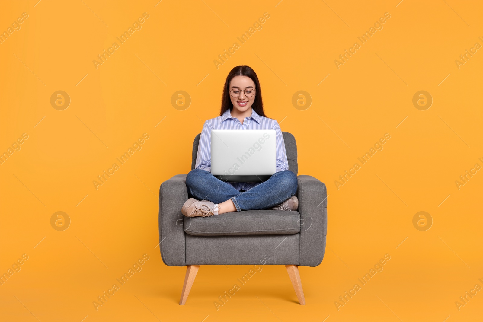 Photo of Smiling young woman working with laptop in armchair on yellow background