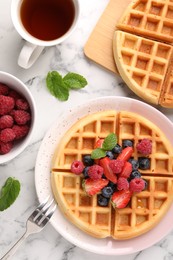 Photo of Tasty Belgian waffles with fresh berries served on white marble table, flat lay