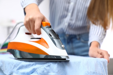 Photo of Young woman ironing shirt on board at home, closeup