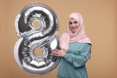 Photo of Happy Women's Day. Woman in hijab with balloon in shape of number 8 on beige background
