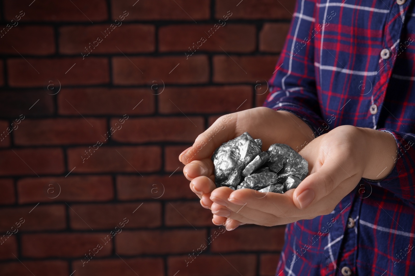 Photo of Woman with silver nuggets against brick background, closeup. Space for text