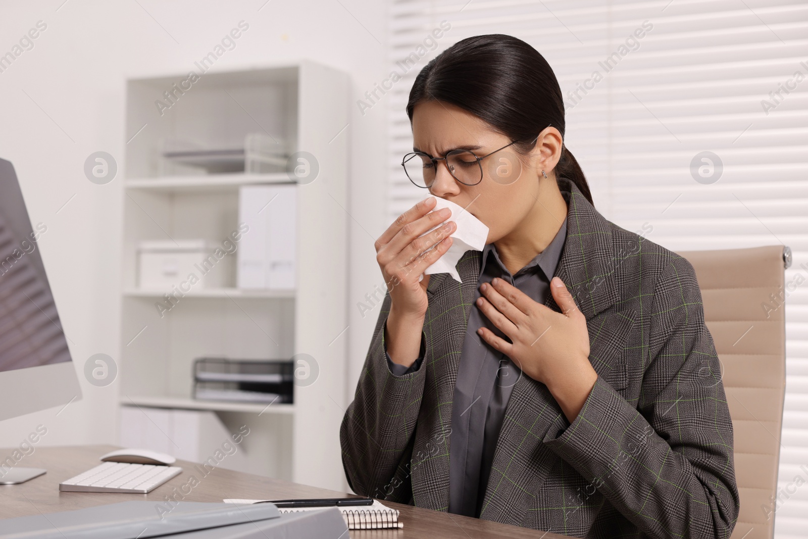 Photo of Woman with tissue coughing at table in office. Cold symptoms