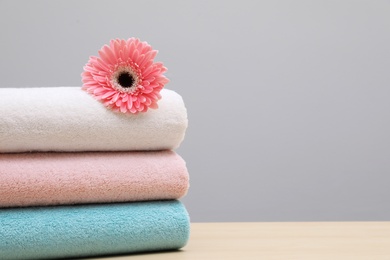 Photo of Stack of fresh towels with flower on table. Space for text