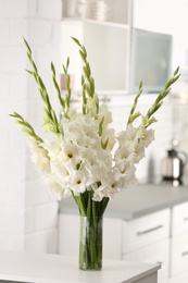 Photo of Vase with beautiful white gladiolus flowers on wooden table in kitchen