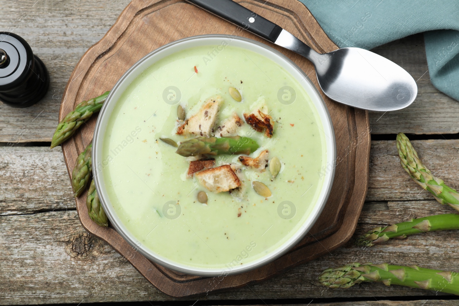 Photo of Bowl of delicious asparagus soup served on wooden table, flat lay