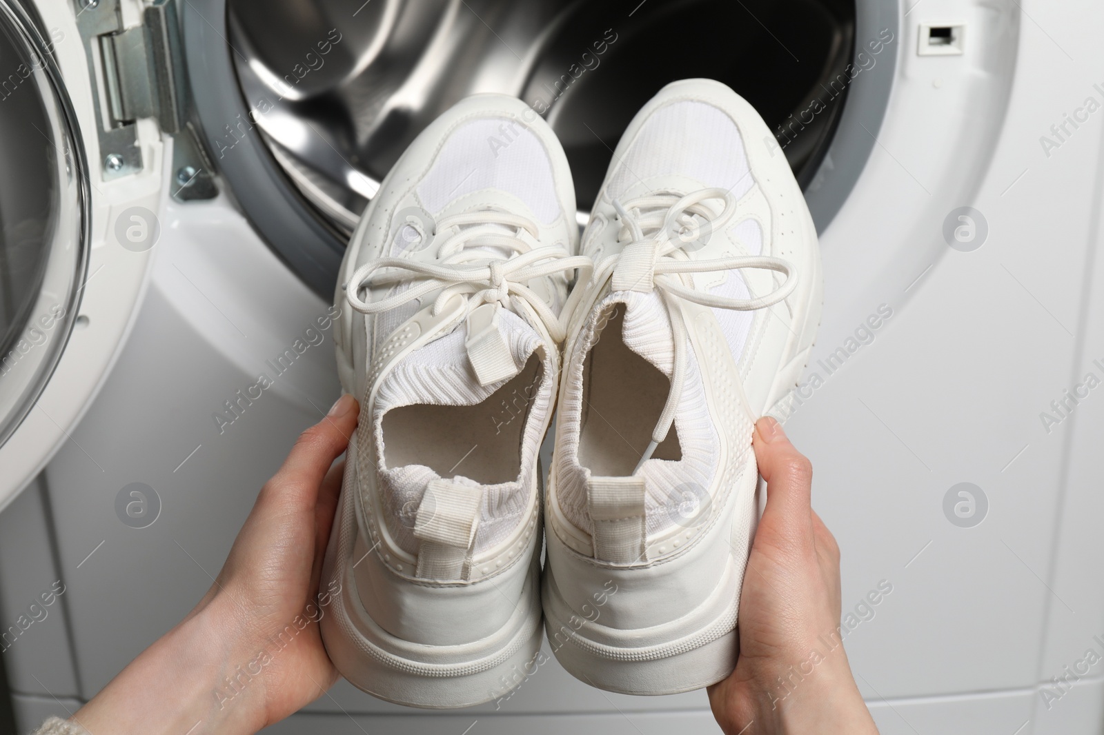 Photo of Woman putting stylish sneakers into washing machine, closeup