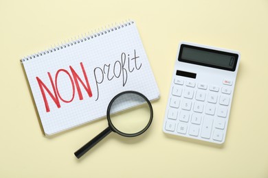 Photo of Notebook with phrase Non Profit, calculator and magnifying glass on beige background, flat lay