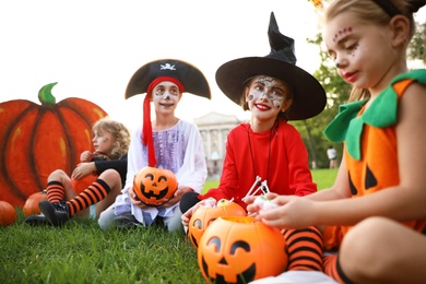 Photo of Cute little kids with pumpkin candy buckets wearing Halloween costumes in park