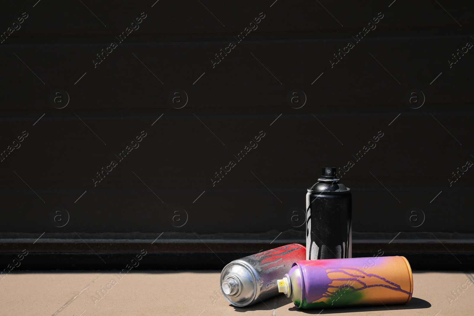 Photo of Used cans of spray paint on tile floor near black wall outdoors, space for text. Graffiti supplies