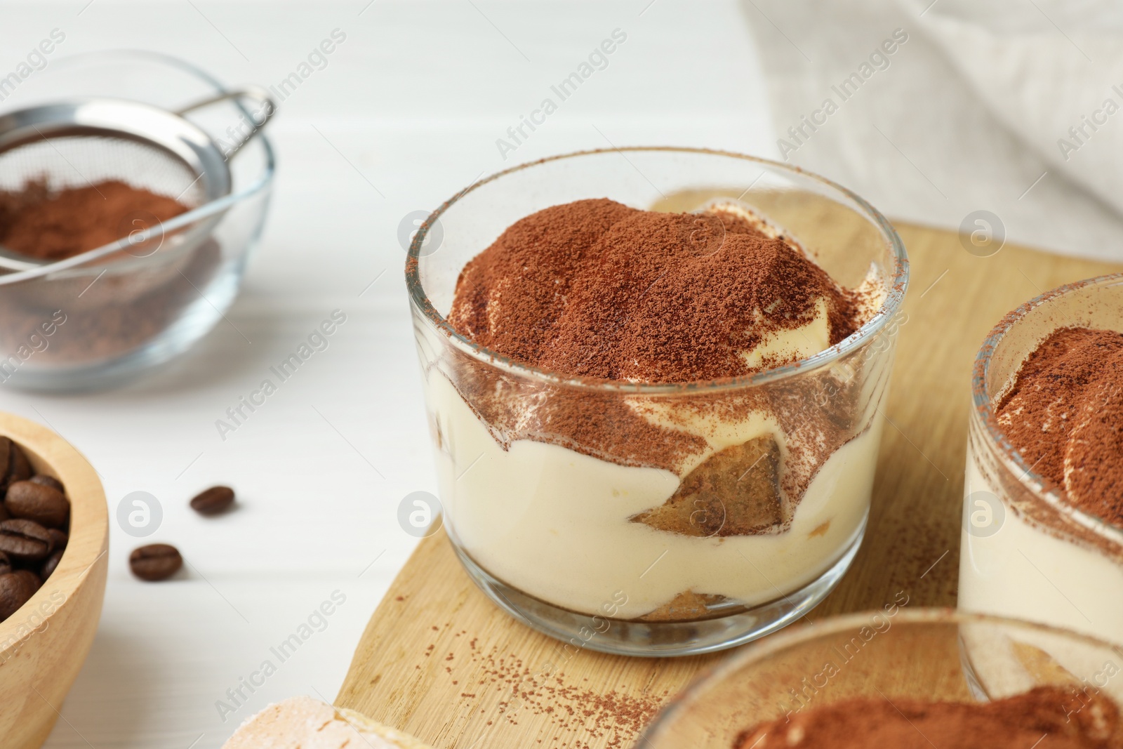Photo of Delicious tiramisu in glasses and coffee beans on white table, closeup