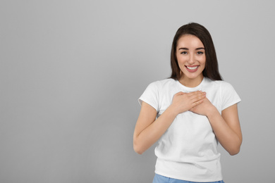 Beautiful grateful woman with hands on chest against light grey background. Space for text