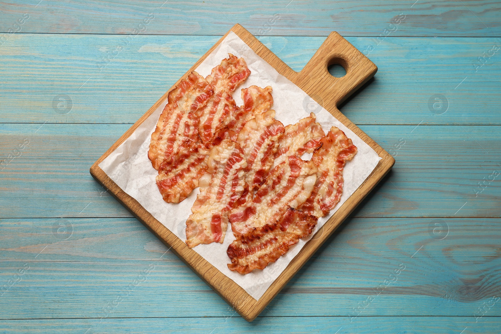 Photo of Delicious fried bacon slices on blue wooden table, top view