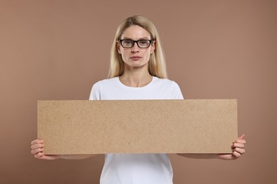 Photo of Woman holding blank cardboard banner on brown background, space for text