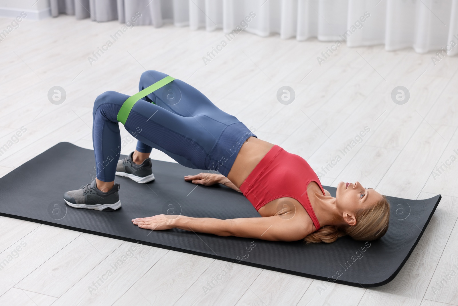 Photo of Athletic woman doing exercise with fitness elastic band on mat indoors