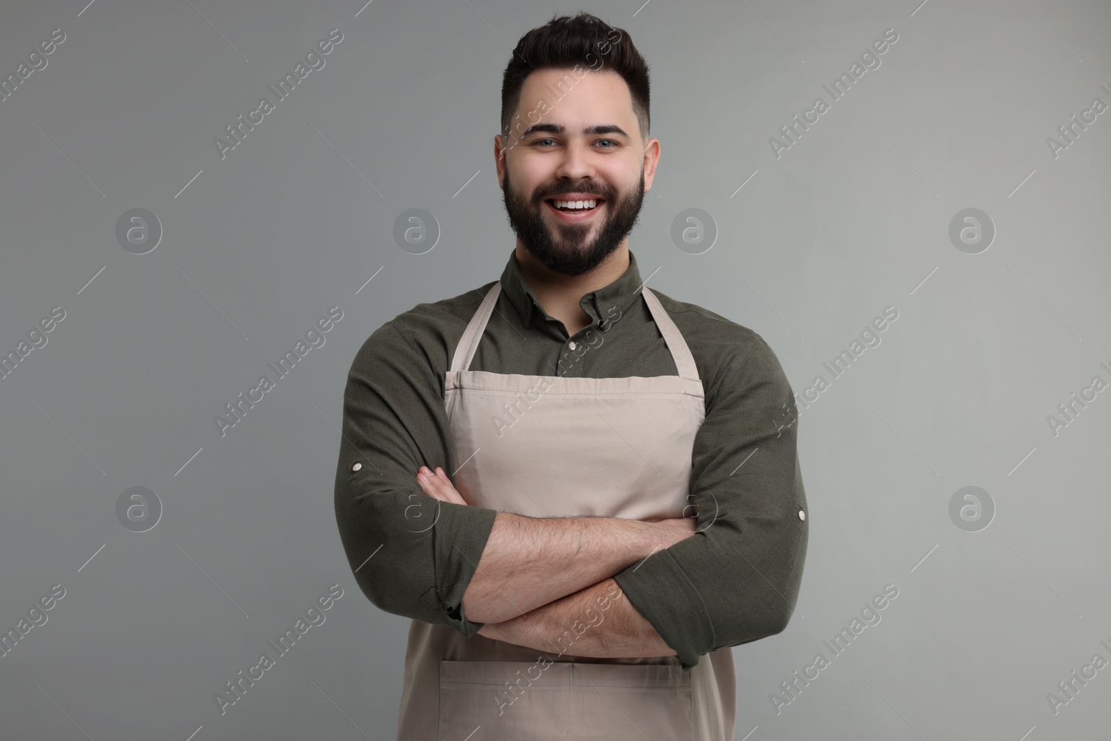 Photo of Smiling man in kitchen apron with crossed arms on grey background. Mockup for design