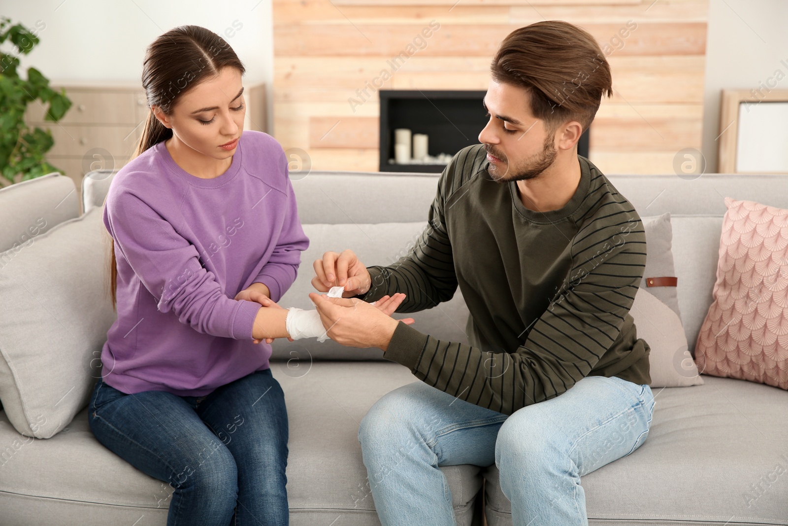 Photo of Young man applying bandage on woman's injured hand at home. First aid