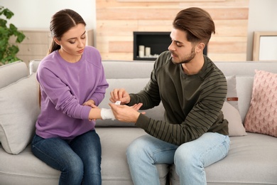 Young man applying bandage on woman's injured hand at home. First aid