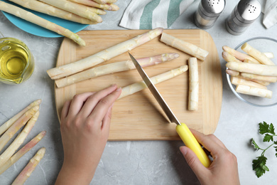 Photo of Woman cutting fresh white asparagus at grey marble table, top view