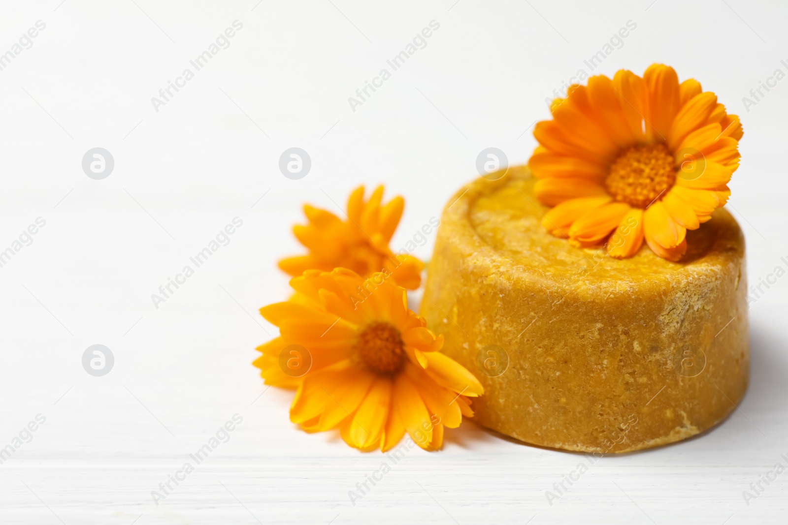 Photo of Yellow solid shampoo bar and flowers on white wooden table, closeup. Space for text