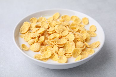 Photo of Breakfast cereal. Corn flakes and milk in bowl on light grey table, closeup