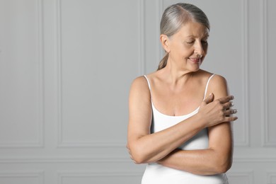 Happy woman applying body cream onto shoulder near white wall. Space for text