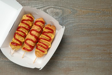 Delicious corn dogs with mustard and ketchup on wooden table, top view. Space for text