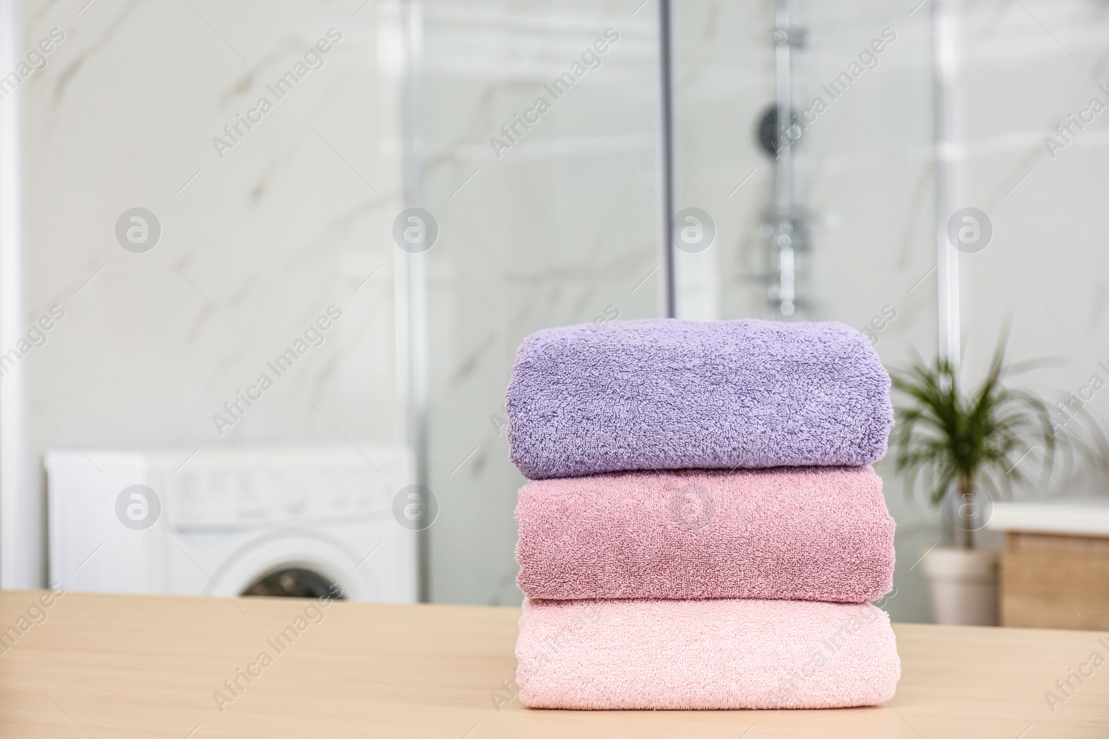 Photo of Stack of fresh towels on wooden table in bathroom. Space for text