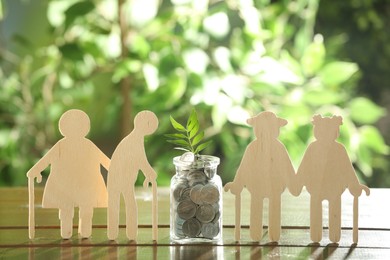 Pension savings. Figures of elderly people, coins and green twig in jar outdoors