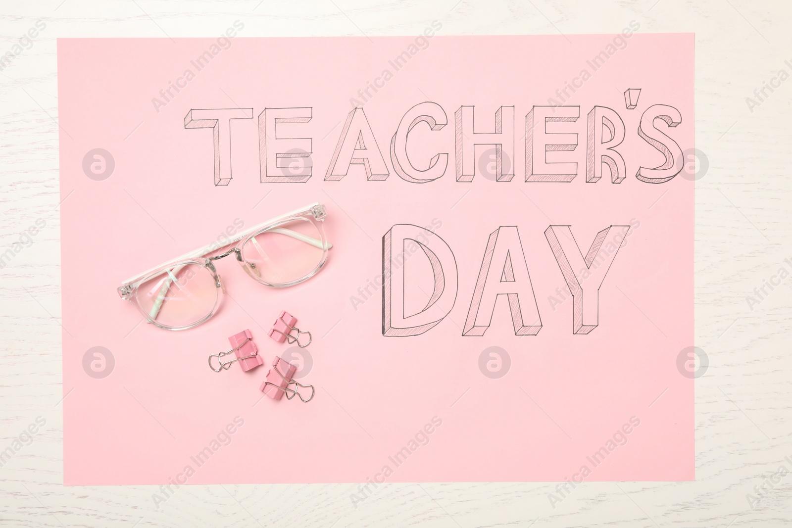 Photo of Sheet of pink paper with words TEACHER'S DAY, glasses and clips on white wooden background, top view