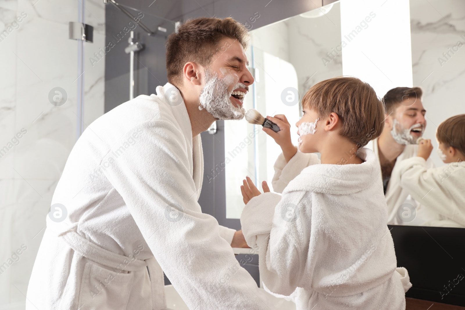 Photo of Dad and son with shaving foam on their faces having fun in bathroom