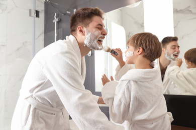 Dad and son with shaving foam on their faces having fun in bathroom