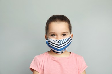 Cute little girl in protective mask on grey background